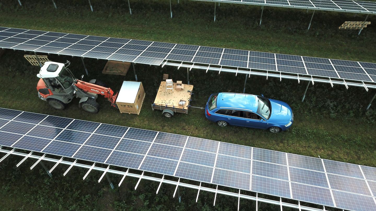 Aerial view of solar panels in a field with a car and tractor driving between them.