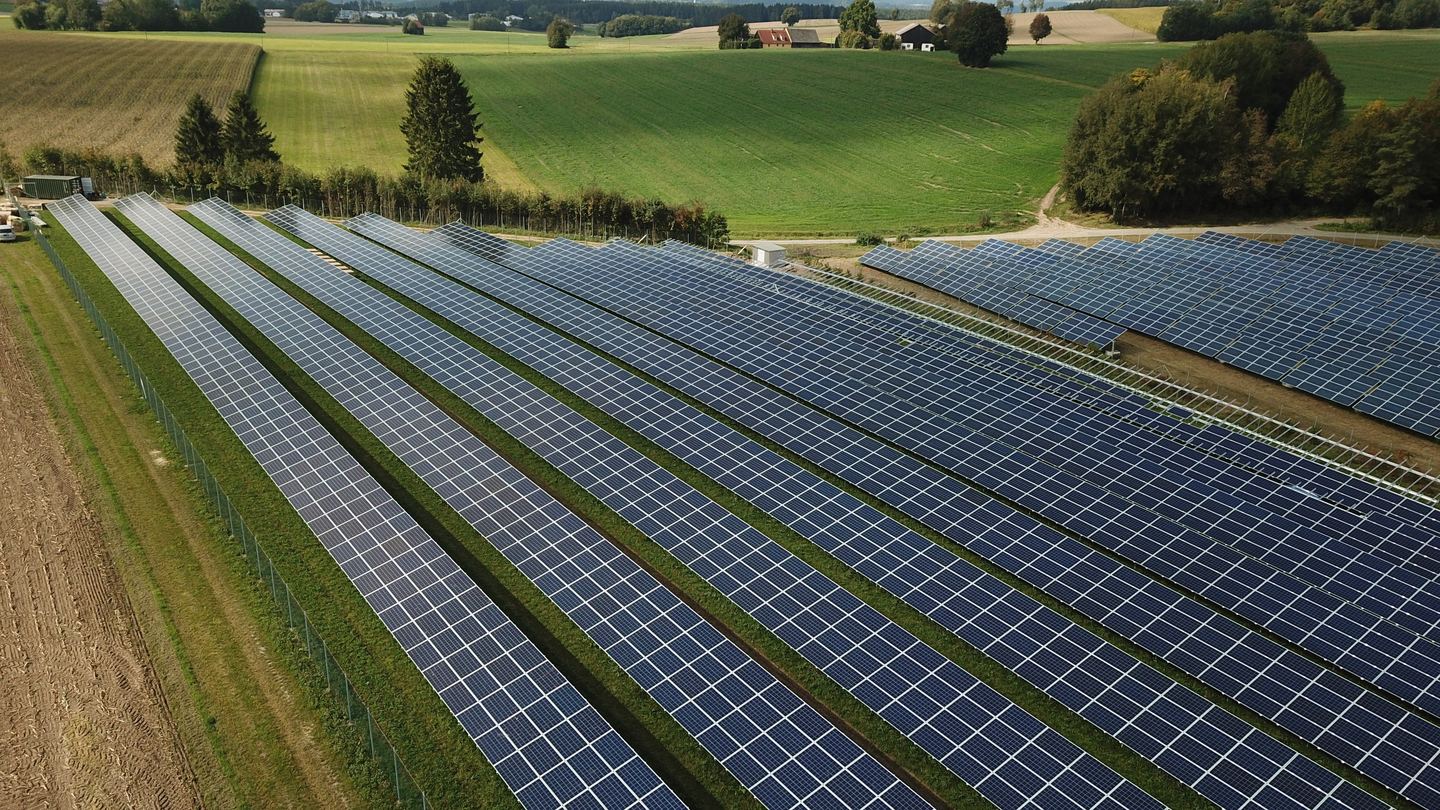 Aerial view of solar panels in a field with a car and tractor driving between them.